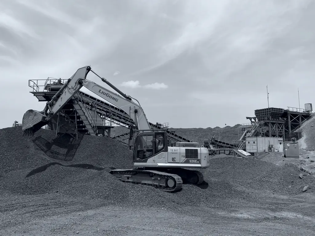 Hydraulic excavator feeding a mobile crushing unit on an ore stockpile